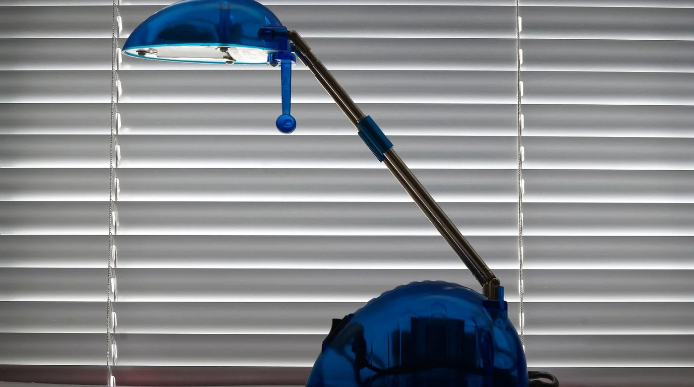 Blaue Gelenklampe vor einer hellen Jalousie